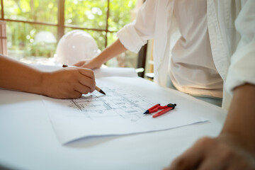 Two people are drawing on a white sheet of paper. One of them is wearing a hard hat