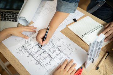 A man and a woman are working on a drawing of a building. The man is using a pen to draw the building, while the woman is looking at the drawing. Scene is focused and collaborative