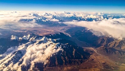 An aerial view of snow-capped mountain range with valley below, blanketed with low-lying clouds under a clear blue sky