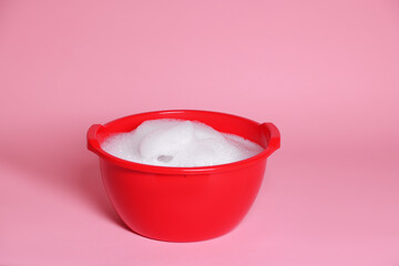Red plastic basin with soapy water on pink background