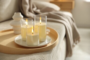 Beautiful LED candles and vase on sofa indoors, closeup. Space for text