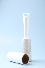 Lint roller with used sticky tape and new adhesive roll on light blue background