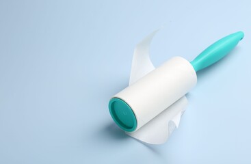 Lint roller with used sticky tape on light blue background, closeup. Space for text