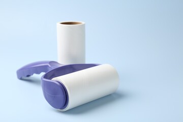 Lint roller and adhesive roll on light blue background, closeup. Space for text