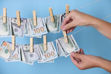 Money laundering. Woman hanging banknote on clothesline against light blue background, closeup
