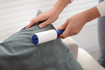 Woman cleaning cushion with lint roller at home, closeup
