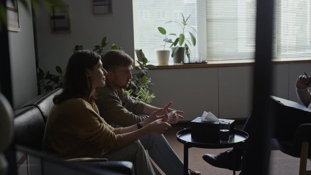 Side view shot of young couple sitting on couch in therapy session and talking resolving conflict and differences, with woman nodding