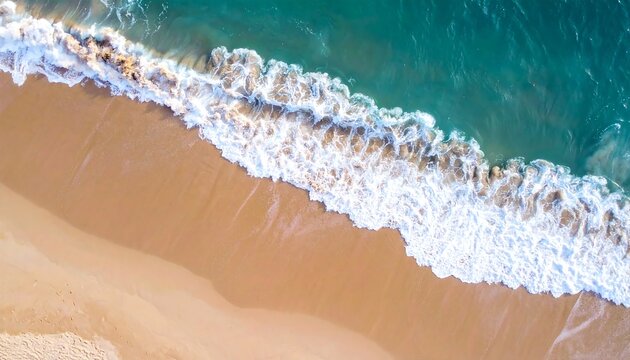 An aerial view presents the meeting of a sandy beach and the ocean. Turquoise and white waves crash onto the shore under sunlight