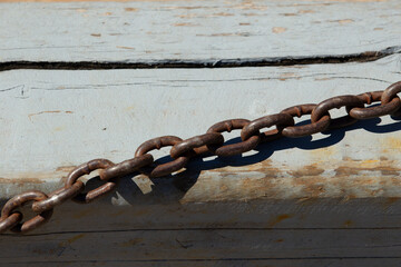 Rusted metal chain lying on weathered wooden surface. Old industrial chain casting shadow on faded paint.
