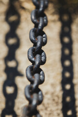 Close-up of dark metal chain casting shadow on concrete. Industrial chain with strong sunlight and sharp shadow.
