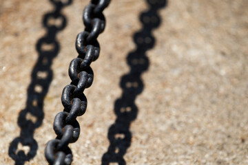 Close-up of dark metal chain casting shadow on concrete. Industrial chain with strong sunlight and sharp shadow.