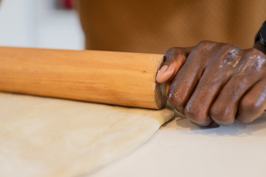 African American man pressing dough with wooden rolling pin on kitchen countertop with flour dust