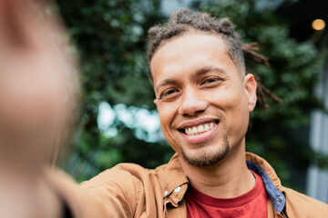 Man taking selfie while smiling in garden with smartphone capturing lush green backdrop