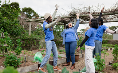 Diverse volunteers tending wooden raised garden beds at community garden with vine-covered trellis