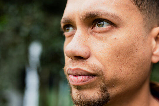 Man gazing toward side outdoors in leafy park wearing dark hoodie during daylight