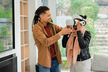 Diverse friends guiding female friend wearing white VR headset beside sofa in living room