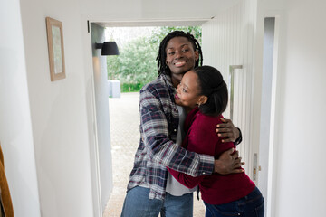 African American couple embracing warmly in home doorway with gravel pathway and lush green bushes
