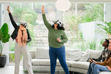 Diverse friends exploring virtual reality wearing headsets in living room with tablet on sofa