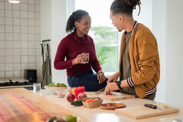 Diverse couple preparing salad on kitchen island with wooden cutting board glass of water and bowls
