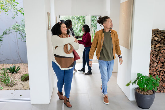 Diverse friends walking through hallway near glazed doors examining art and firewood niche