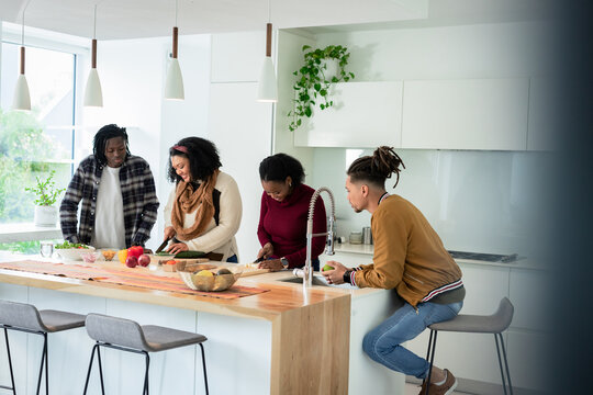 Diverse friends chopping vegetables and holding fruit on wooden kitchen island under pendant lights
