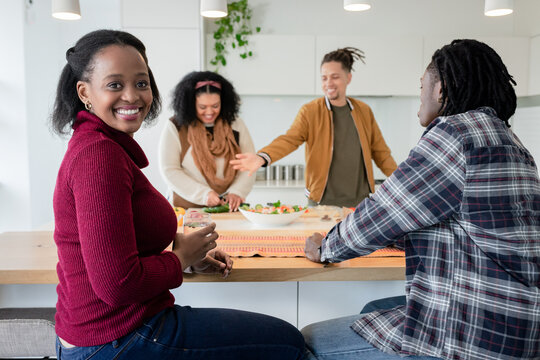 Diverse friends preparing salad at kitchen counter holding glass of water and chatting, copy space