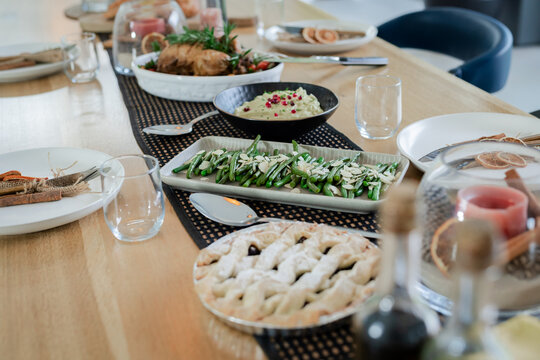 Dining table is showcasing lattice pie, green beans, roasted meat and glass dome in dining room