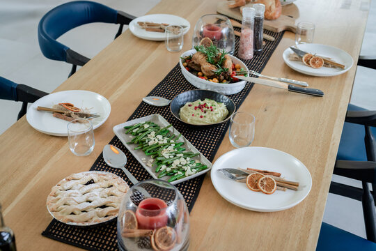 Wooden table featuring black runner with roast chicken, avocado dip, green beans, fruit pie