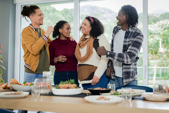 Diverse friends standing around dining table at home with salad and bread, chatting, smiling