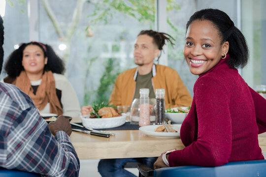 Diverse friends sharing meal around wooden dining table by window with salad and carafe, copy space