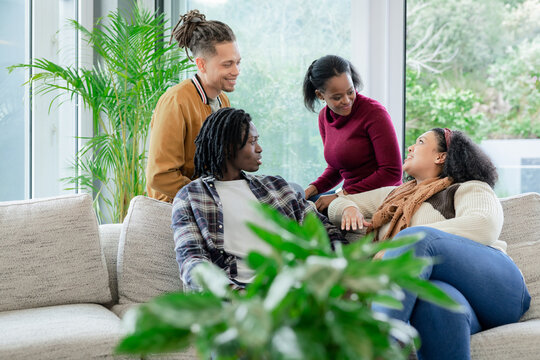 Diverse friends chatting and relaxing on sectional sofa in modern living room with potted plant - Powered by Adobe