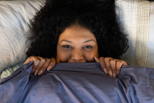 Woman lying on bed in bedroom, resting head on white pillow and gripping blue duvet