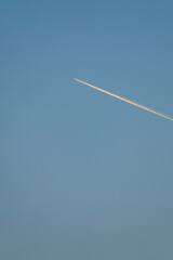 Airplane jet leaving long bright contrail in clear sky vertical