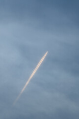 Bright airplane contrail cutting through soft blue sky vertical