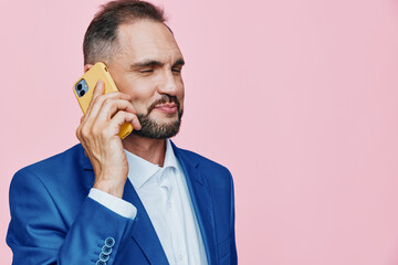 Professional man in a blue suit talks on a yellow phone against a solid pink background, projecting...
