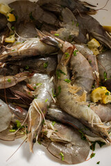 Raw fresh shrimps in plate next to reddened boiled crustaceans in boiling pan. Cooking seafood rich in protein in kitchen by boiling in water. Close up of process of thermal processing of shellfish.