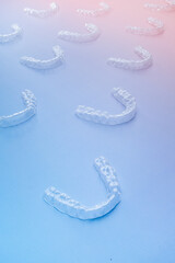 Transparent orthodontic aligners arranged in perspective on pastel blue and pink gradient background, symbolizing modern dental technology, aesthetic healthcare, and orthodontic treatment concept for 