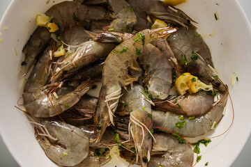 Raw fresh shrimps in plate next to reddened boiled crustaceans in boiling pan. Cooking seafood rich in protein in kitchen by boiling in water. Close up of process of thermal processing of shellfish.