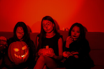 Three girls are celebrating Halloween by holding pumpkins in a dimly lit room.