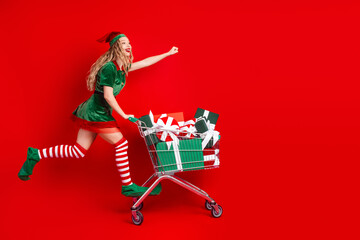Festive elf pushing a shopping cart full of Christmas gifts on a red background, celebrating the holiday spirit with joy.