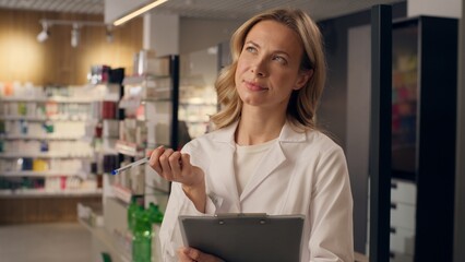 Woman pharmacist writing medicine inventory at pharmacy doctor thoughtful Caucasian girl write...