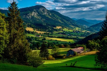 Lush green fields stretch across the landscape, dotted with trees and a rustic barn. Majestic mountains rise in the background under a partly cloudy sky