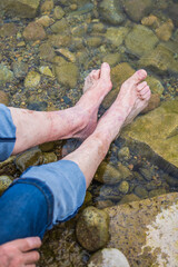Elderly man cooling tired and swollen feet in a natural river or lake and relaxing