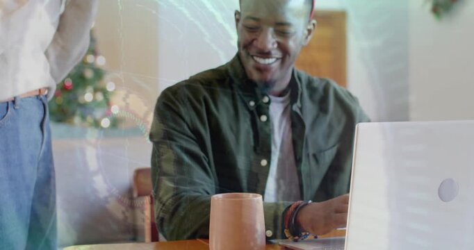 Man working remotely on laptop when woman carrying mug fitting candy cane headband and hugging