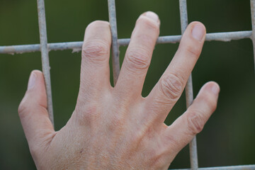 Hand grasping metal fence expressing confinement and despair
