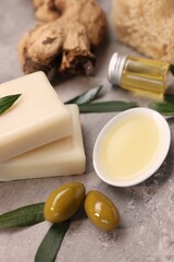 Handmade soap bars, olives, green leaves and oil on gray textured table, closeup