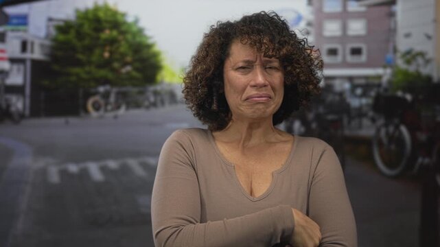 Woman pinches nose on city street displaying discomfort at strong smell near bicycles and parked cars alongside buildings; disgust.