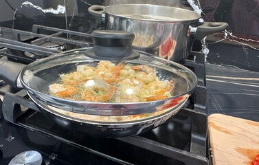 Shrimps and pasta cooking on stove in kitchen, closeup