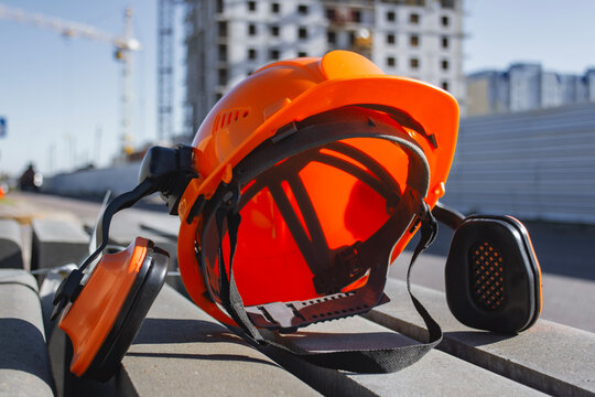 Yellow safety helmet with attached ear defenders lying on concrete blocks at a construction site. Concept workplace safety, industrial protection gear and professional equipment used by builders.
