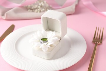Beautiful table setting for romantic dinner and box with engagement ring on pink background, closeup